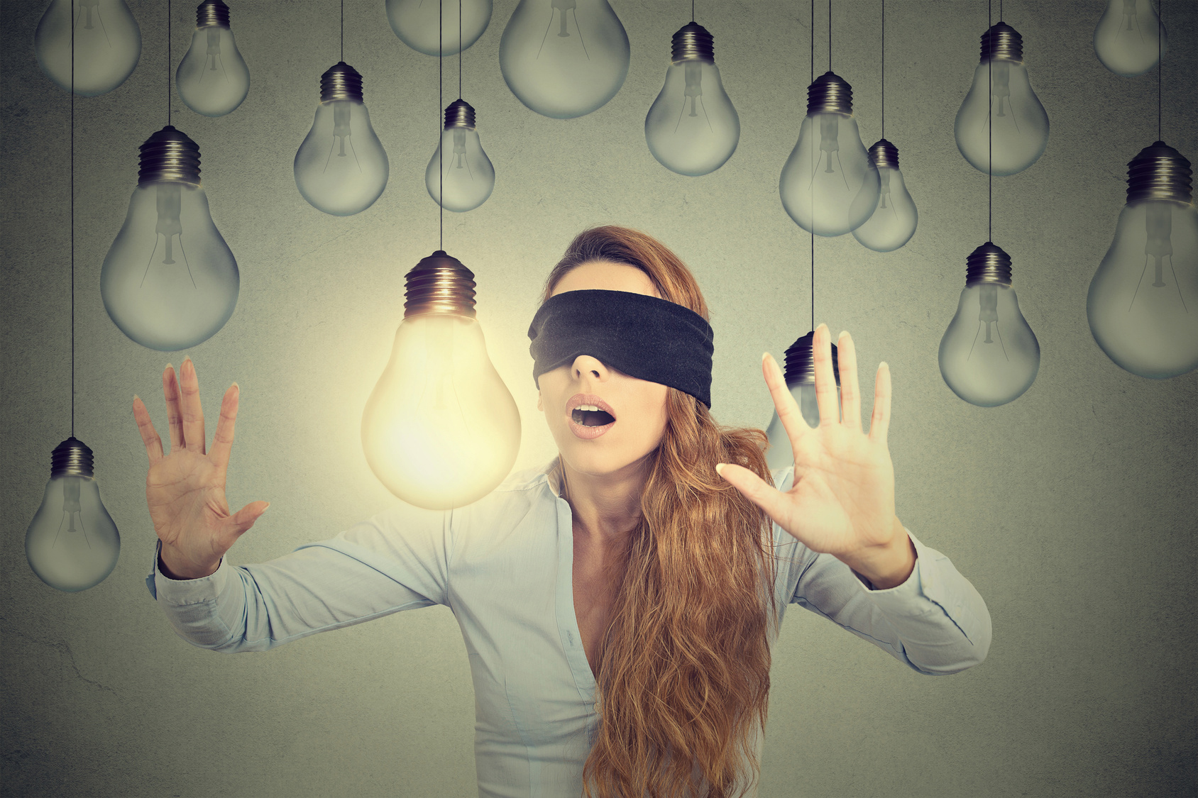 Blindfolded young woman walking through lightbulbs searching for